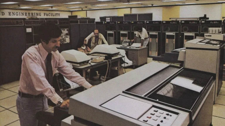 Sala de mainframe dos anos 1970 com operadores e plotador — capa sobre sistemas legados